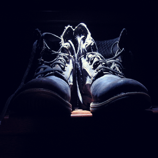 A pair of black leather boots, lit by a spotlight overhead.