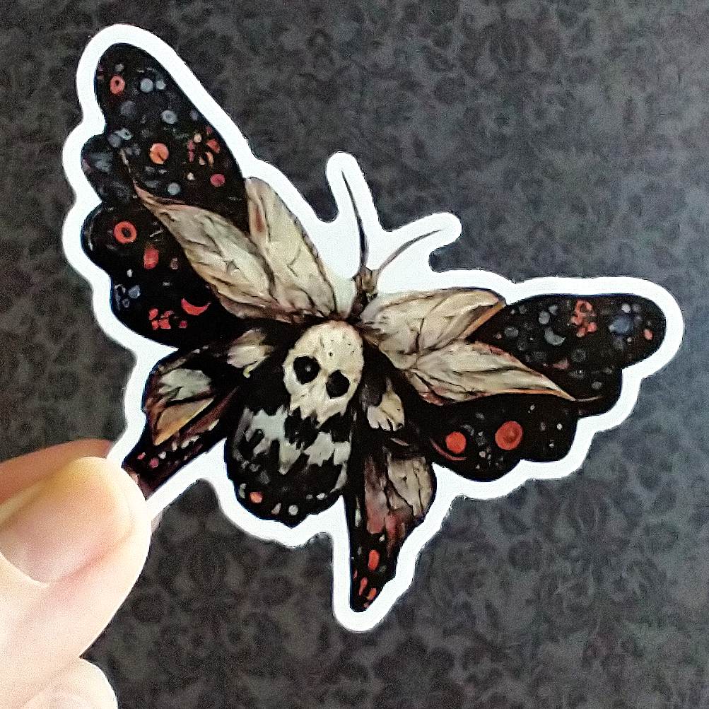 A hand holding a folk art inspired sticker of a Death's Head Moth, with a white background.