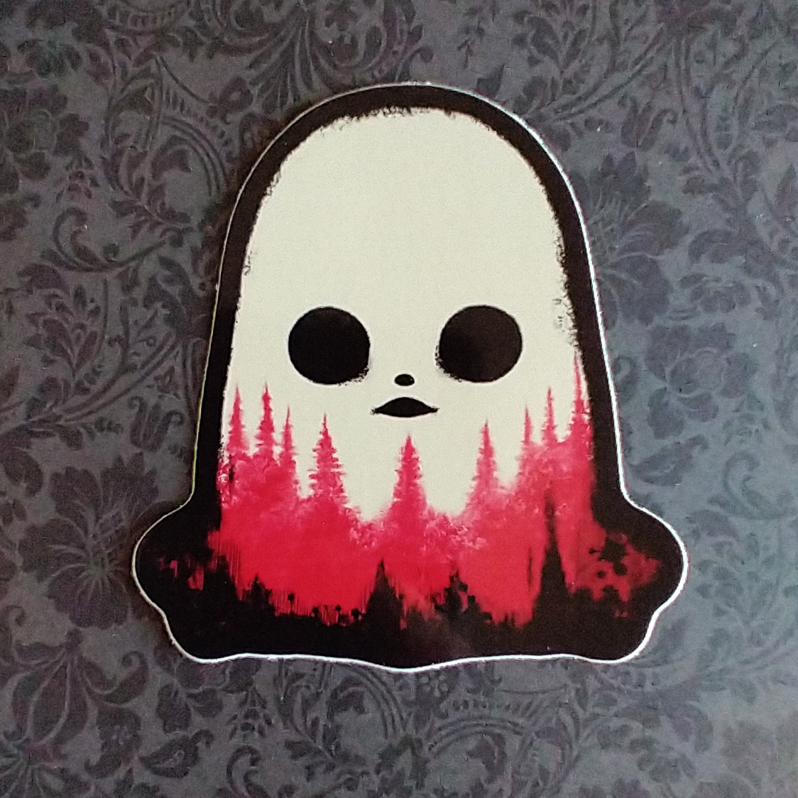 A black, white, and red sticker of a ghost with pine trees along the bottom. The ghost's mouth looks like a flying saucer, and the pine trees look a bit like blood.