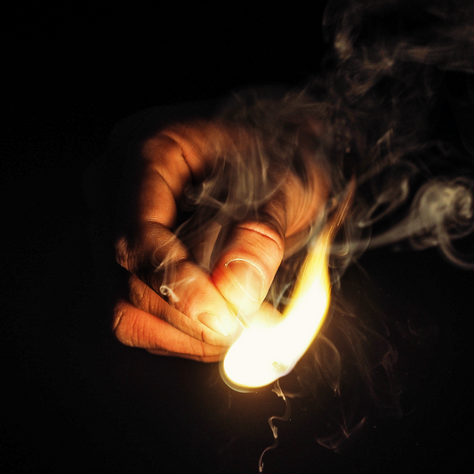 A hand striking a match, which makes plenty of smoke.