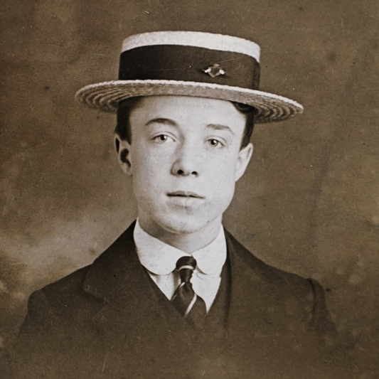 An antique photograph of a boy wearing a suit and a boater hat.