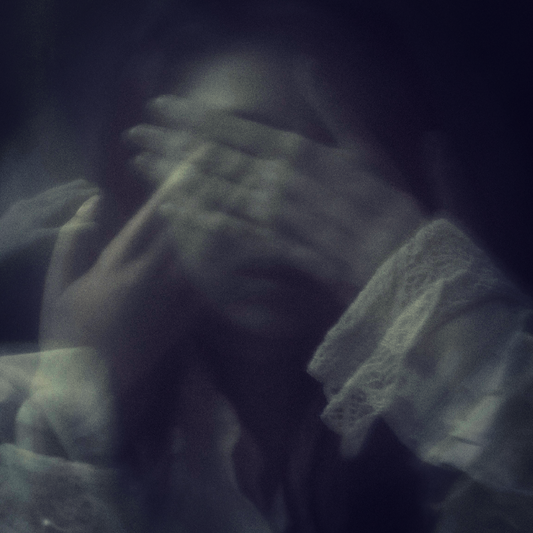 A dark, ghostly double exposure photograph of a woman with her hands covering her eyes.