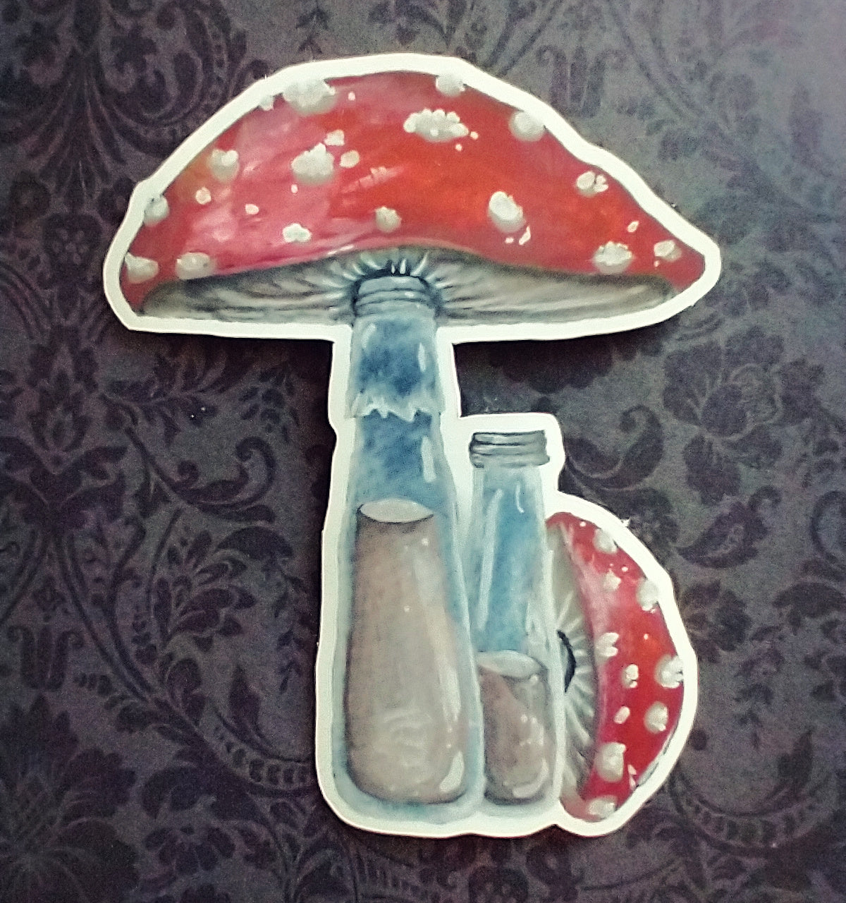 A sticker of a large milk bottle topped with a mushroom cap that's red with white spots. Another similar bottle sits next to it, this one with its cap removed and set alongside.