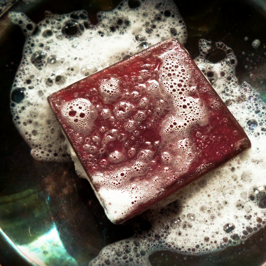A square, burgundy bar of soap, surrounded by suds.