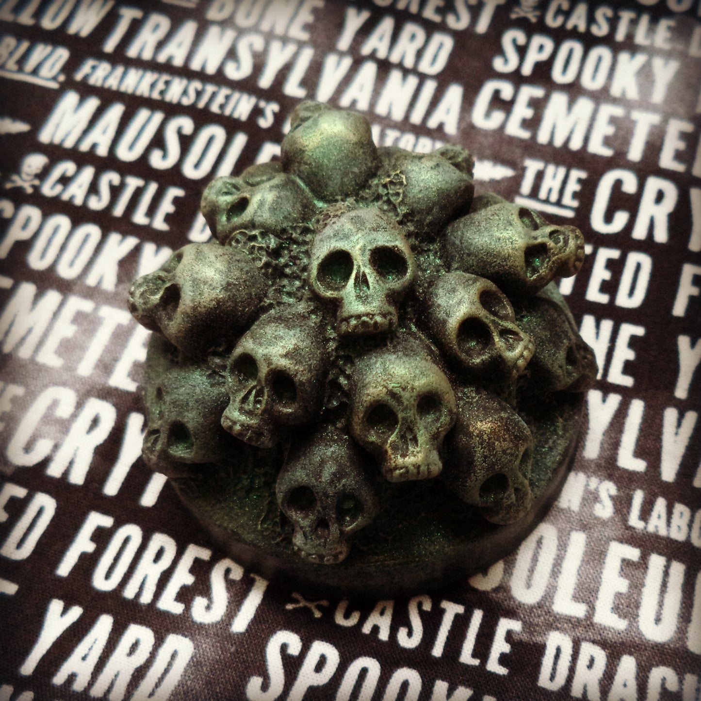 A Catacomb soap: many small skulls, tinted a pearly green. It is sitting on Halloween fabric printed with the names of spooky places.
